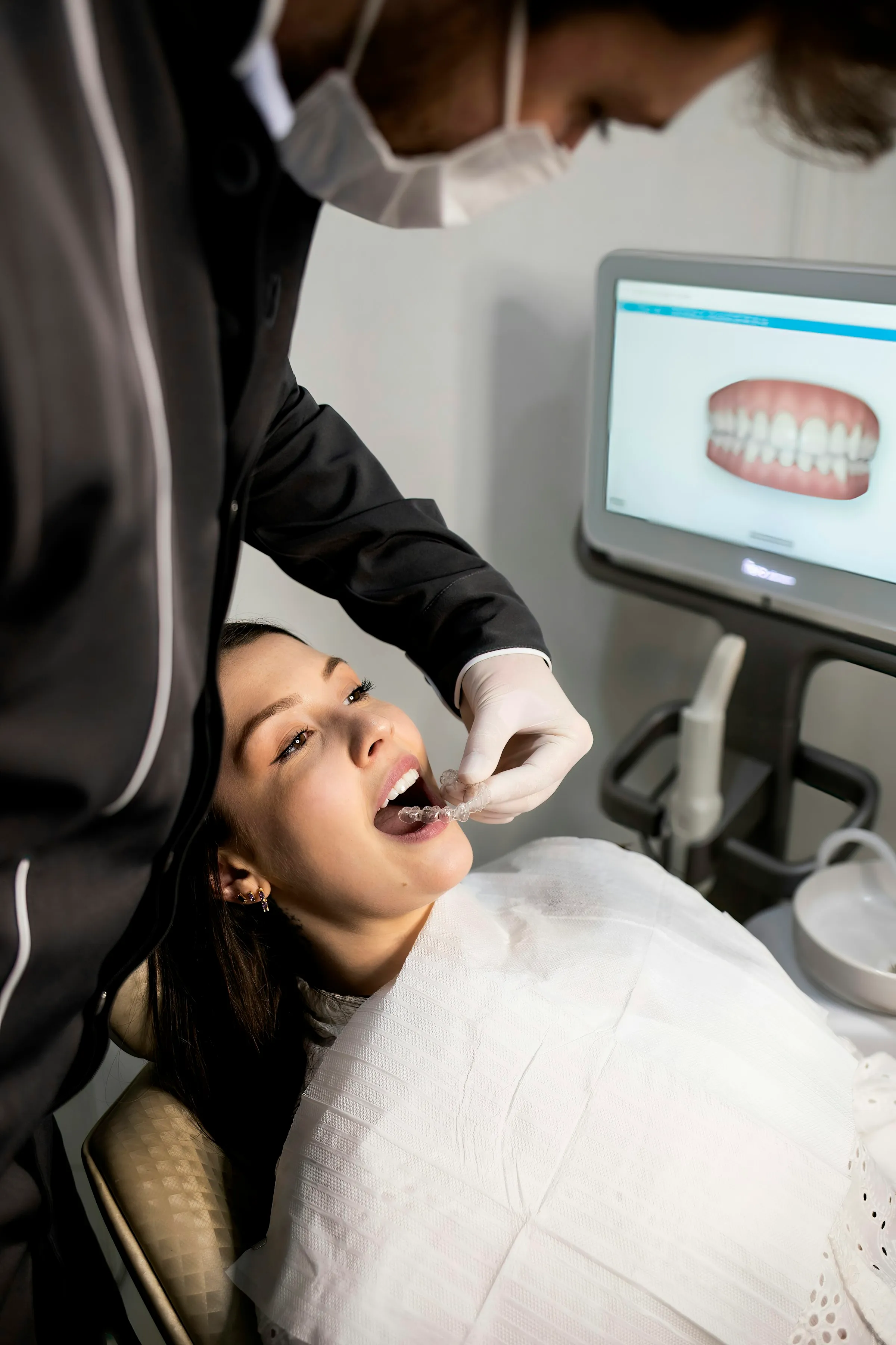 Zahnarzt bei der Behandlung einer Patientin, im Hintergrund ein digitaler 3D-Scan der Zähne auf dem Monitor